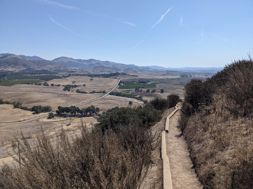 A dry and mostly treeless valley, viewed from a small dirt hill reinforced with wood.